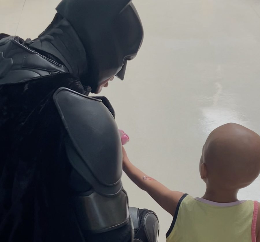 Batman Thyago sentado ao lado de uma criança internada